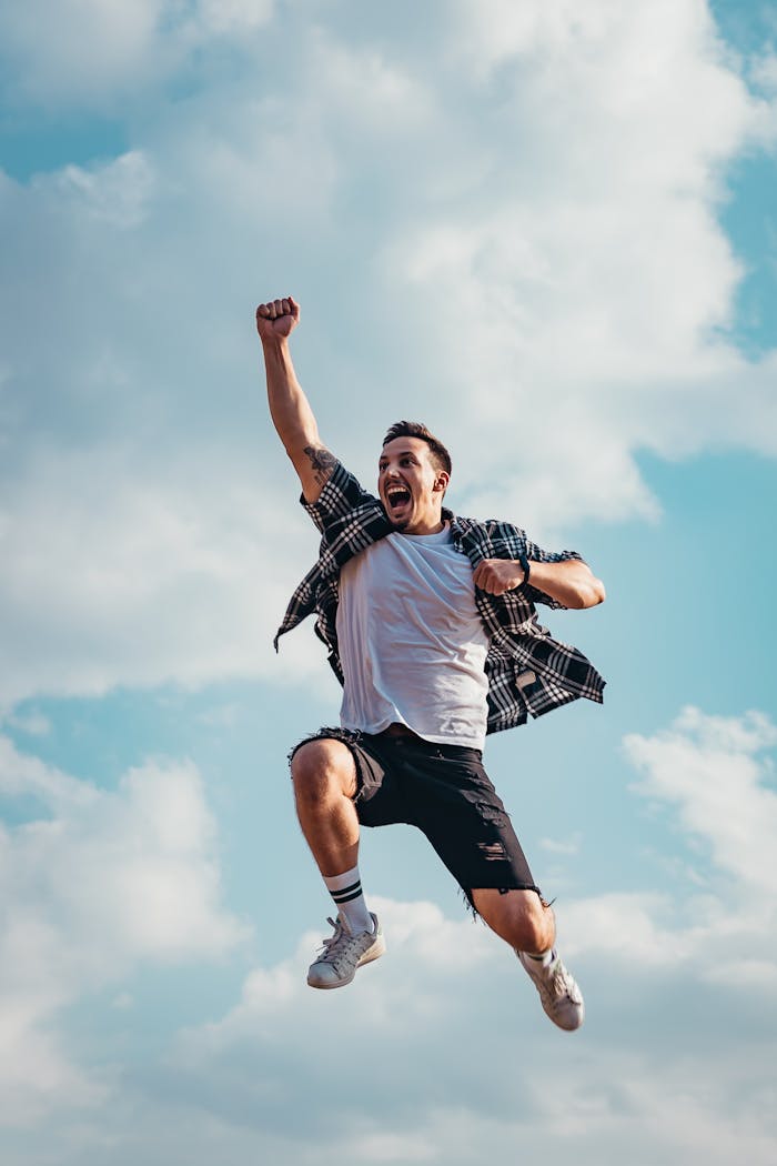 gallery-04 A joyful young man jumps midair with clouds and blue sky in the background, exuding energy and freedom.