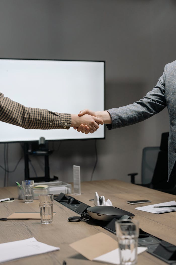 featured-images-03 Two business professionals shaking hands in a modern meeting room, symbolizing successful collaboration.